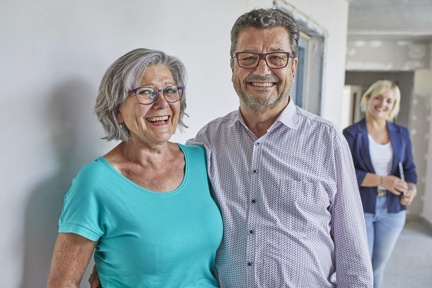 Zufriedenes Paar bei Immobilienbesichtigung von Becker Immobilien Lachendes älteres Paar posiert in neuer Immobilie, im Hintergrund steht eine Beraterin von Becker Immobilien